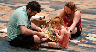 A family sits together on the carpet reading from a Braille book.